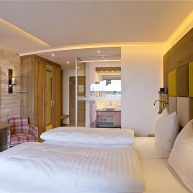 A modern hotel room with two beds, a television, and comfortable armchairs. The warm colors and stylish decor create an inviting atmosphere.