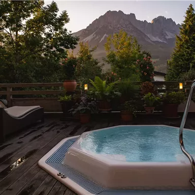 Ein Whirlpool auf einer Terrasse mit Blick auf die Berge. Grüne Pflanzen und gemütliche Liegen runden die entspannende Atmosphäre ab.