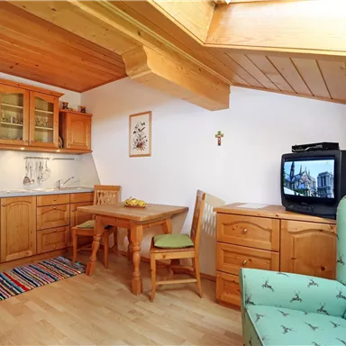 Eine gemütliche Ferienwohnung mit Holzfußboden und einer Küchenzeile. Ein Esstisch und ein Fernseher sind ebenfalls vorhanden.