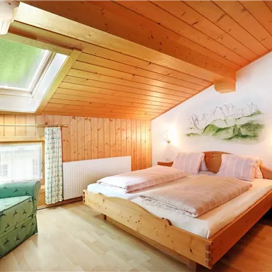 Ein gemütliches Schlafzimmer mit Holzverkleidung. Es gibt ein großes Bett, einen Sessel und ein Fenster mit natürlichem Licht.