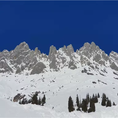 An impressive mountain landscape with snow-covered peaks and clear blue sky. Green fir trees blend into the winter scene.