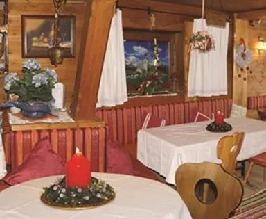 Ein gemütliches Restaurant mit Holzelementen und traditioneller Einrichtung. Die Tische sind schön gedeckt und es gibt eine warme, einladende Atmosphäre.