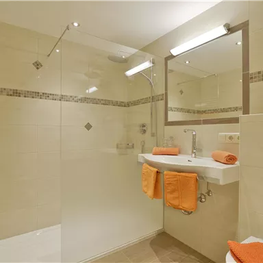 A modern bathroom with a shower and a sink. Orange towels give the room a fresh touch.