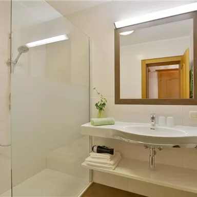 A modern bathroom with a shower and sink. The room is designed to be bright and welcoming.