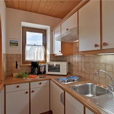 A bright kitchen with a wooden ceiling and modern appliances. The room is well equipped with a sink, microwave, and a window that lets in plenty of daylight.