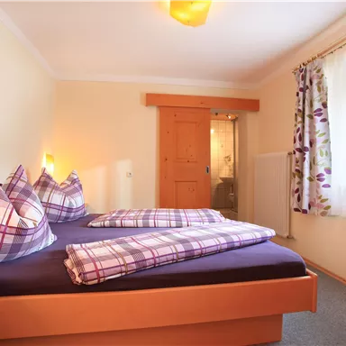 A cozy bedroom with a double bed and checkered pillows. The walls are painted in soft colors, and a window provides plenty of natural light.