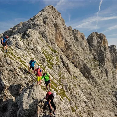 Eine Gruppe von Bergsteigern erklimmt einen felsigen Gipfel. Die Landschaft ist majestätisch mit klaren blauen Himmel im Hintergrund.