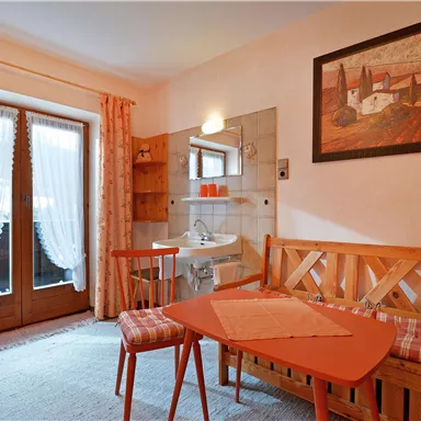 Ein gemütlicher Raum mit einem kleinen Tisch und Stühlen. Die Fenster sind mit Vorhängen dekoriert und es gibt ein schönes Bild an der Wand.