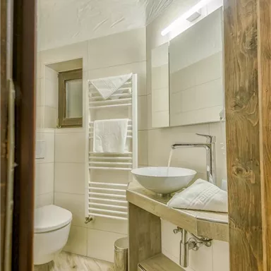 Ein modernes Badezimmer mit hellen Fliesen und Holzdetails. Es verfügt über ein Waschbecken, eine Toilette und einen Handtuchhalter.