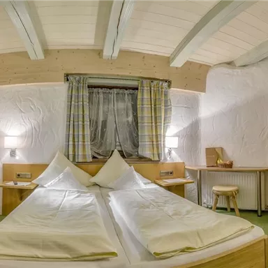 Ein gemütliches Schlafzimmer mit zwei Betten, weißen Bettwäsche und Holz-Möbeln. Die Wände sind schlicht gestaltet und das Licht ist warm und einladend.