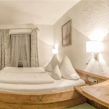 Ein gemütliches Schlafzimmer mit einem großen Doppelbett und einer warmen Holzdeko. Neben dem Bett steht ein Tisch mit einer Obstschale.