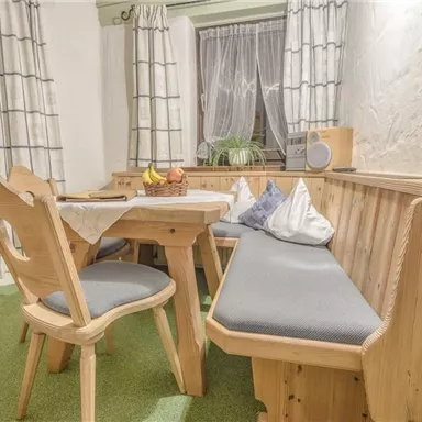 Ein gemütlicher Essbereich mit Holzmöbeln und einer gepolsterten Bank. Große Fenster lassen viel Licht herein und schaffen eine einladende Atmosphäre.