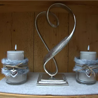 Two decorative candles in jars with gray ribbons stand next to an elegant, curved metal figure. The background is made of wood, creating a cozy atmosphere.