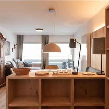 Ein modern eingerichteter Wohnraum mit einer Holztheke und einem großen Fenster. Im Hintergrund sind ein bequemes Sofa und ein antiker Schrank zu sehen.