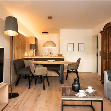 Ein modernes Wohnzimmer mit einer gemütlichen Couch und einem Esstisch. Es gibt einen Fernseher, Stühle und eine stilvolle Stehlampe.