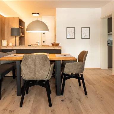 Ein modernes Esszimmer mit einem Holztisch und gemütlichen Stühlen. Die Wände sind in neutralen Farben gehalten und das Licht ist angenehm warm.