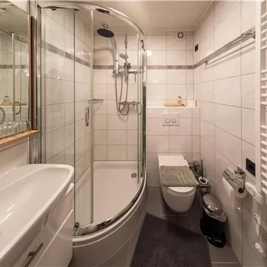 Ein modernes Badezimmer mit einer Duschkabine, Waschbecken und Toilette. Die Wände sind mit weißen Fliesen gefliest und es gibt einen Handtuchwärmer.