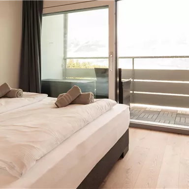 Ein helles Zimmer mit zwei Einzelbetten und einem Balkon. Große Fenster lassen viel Licht herein und bieten einen Blick ins Freie.