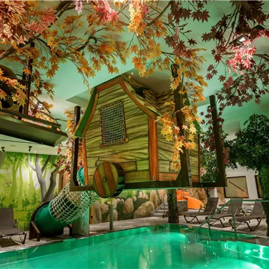 Ein Innenbereich mit einem Pool und einem Baumhaus, das von bunten Blättern umgeben ist. Die Atmosphäre ist kindgerecht und spielerisch gestaltet.