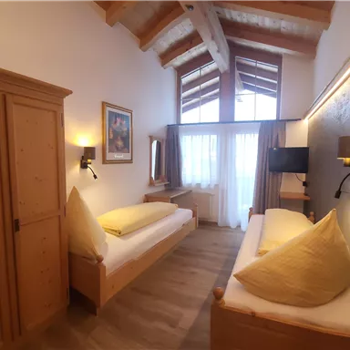 Ein gemütliches Zimmer mit Holzdetails und zwei Einzelbetten. Große Fenster sorgen für viel Tageslicht.