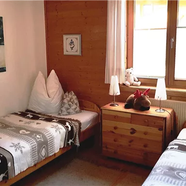 A cozy room with two single beds and wood paneling. The window lets in plenty of daylight and creates an inviting atmosphere.