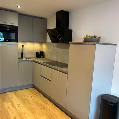 Eine moderne Küche mit grauen Schränken und Holzfußboden. Sie ist gut ausgestattet mit einem Herd, einer Spüle und einem kleinen Tisch.