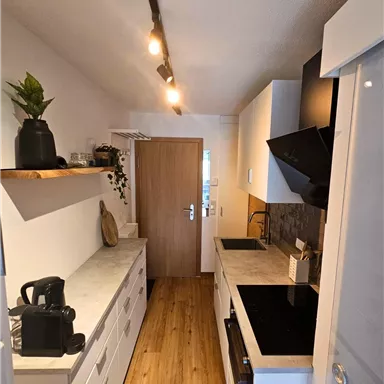A modern kitchen with a bright wooden floor and white furniture. The walls are plain, and there is pleasant lighting.