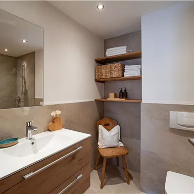 Ein modernes Badezimmer mit Holzschränken und einem klaren Waschbecken. Die Ausstattung umfasst Regale mit Handtüchern und Pflegeprodukten.