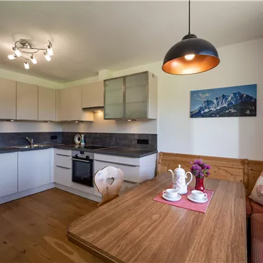 Eine moderne Küche mit hellen Schränken und einer Holzbank. Auf dem Tisch steht ein Teeservice und eine Blumenvase.