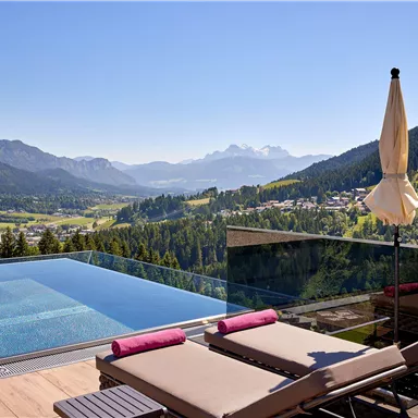 A modern infinity pool with a view of the mountains. Loungers and a sun umbrella complete the relaxing atmosphere.
