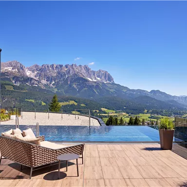 An elegant outdoor area with an infinity pool and mountain views. Clear blue skies and modern furniture create a relaxing atmosphere.