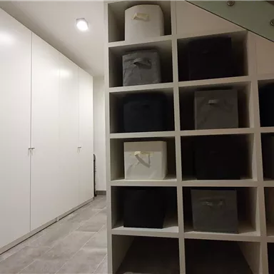 A modern room with white cabinets and a shelving system. The shelf contains colorful storage boxes.