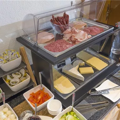 Ein reichhaltiges Frühstücksbuffet mit verschiedenen Wurst- und Käsesorten. Dazu gehören auch kleine Schalen mit Gemüse, Marmelade und Saucen.