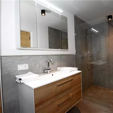 Ein modernes Badezimmer mit einer großen Dusche und einem stilvollen Waschbecken. Die Wände sind in neutralen, grauen Tönen gehalten.