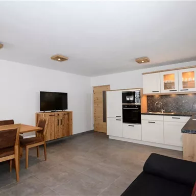 Eine moderne Küche mit Essbereich in einem hellen Raum. Die Einrichtung ist schlicht und funktional mit Holz- und schwarzen Akzenten.