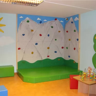 A colorful playroom with a climbing wall motif and a sunny wall. There are various toys and seating options for children.