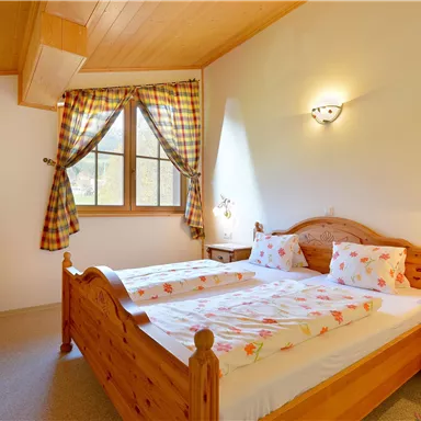 A cozy bedroom with wooden furniture and a large window. The beds are decorated with colorful bed linens and pillows.