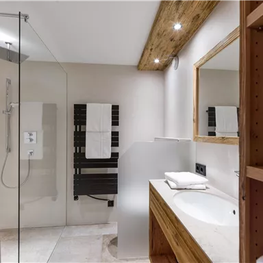 Ein modernes Badezimmer mit einer Glasdusche und Holzakzenten. Es gibt Handtücher und einen weißen Waschbeckenbereich.