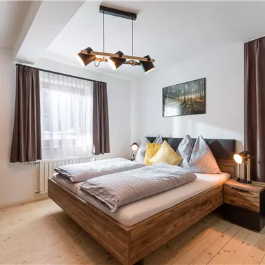 A modern bedroom with a wooden bed and two separate mattresses. The windows let in a lot of light and the walls are painted in neutral colors.