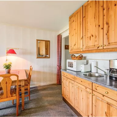 A cozy kitchen with wooden cabinets and a dining table. The rooms have a warm, friendly atmosphere.