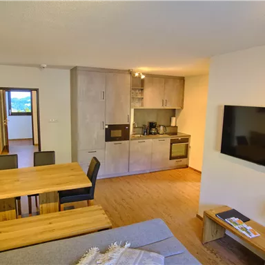 Eine moderne Wohnung mit offenem Wohn- und Küchenbereich. Der Raum verfügt über einen Esstisch, eine Couch und einen Fernseher.