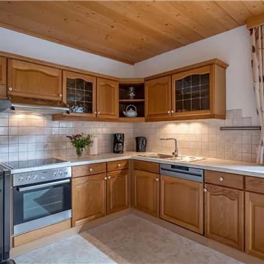 Eine gemütliche Küche mit Holzschränken und modernen Geräten. Die warmen Farben und das Fenster sorgen für eine einladende Atmosphäre.