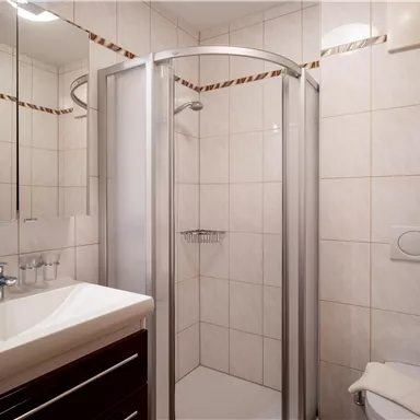 A modern bathroom with a shower and a sink. The walls are tiled and there is a mirror above the sink.