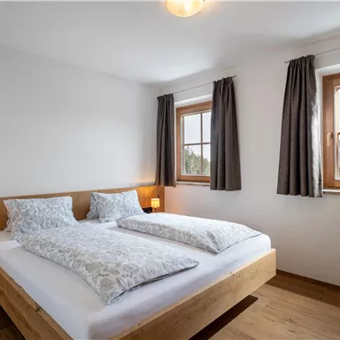 A bright bedroom with two beds and large windows. Wooden details and curtains create a cozy atmosphere.