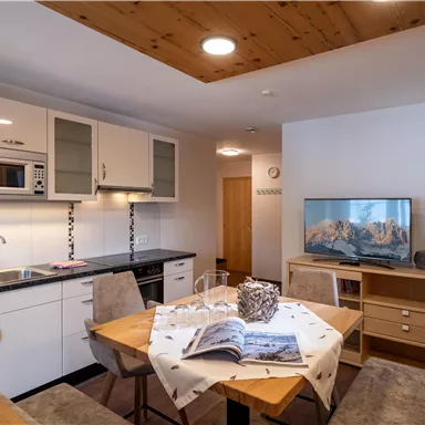A modern apartment with an open kitchen and dining area. The space is bright and inviting, with a television and comfortable furniture.