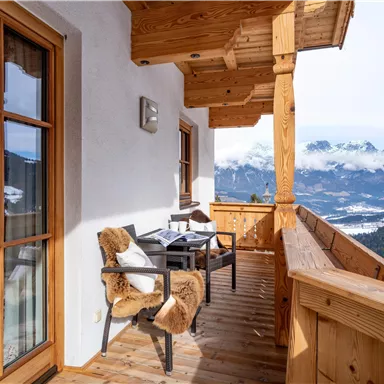 A beautiful balcony with wooden cladding and two cozy chairs. In the background, snow-covered mountains and a clear sky can be seen.