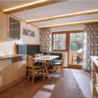 A cozy kitchen with modern appliances and a dining table. Large windows provide a view of the outdoors.