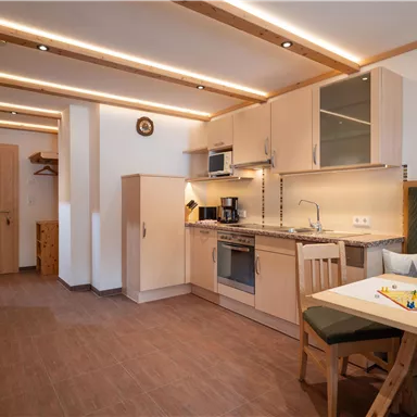 A modern kitchen with light cabinets and a dining area. The room is well-lit and friendly designed.