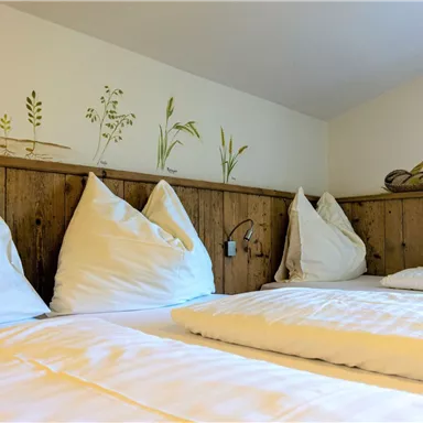 Ein gemütliches Zimmer mit zwei Betten und kissen. Die Wände sind mit natürlichen Motiven dekoriert.