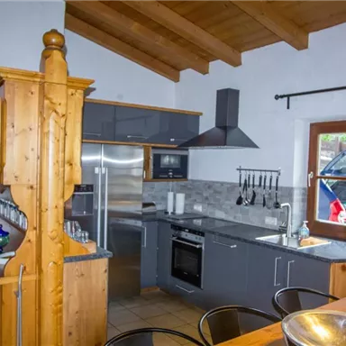 Eine moderne Küche mit Holz- und Grautönen. Sie ist gut ausgestattet und hat große Fenster für viel Licht.